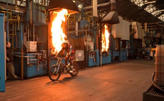 1a) 12 times Trials World Champion, Dougie Lampkin, rides past flaming furnaces at Wallwork Heat Treatment